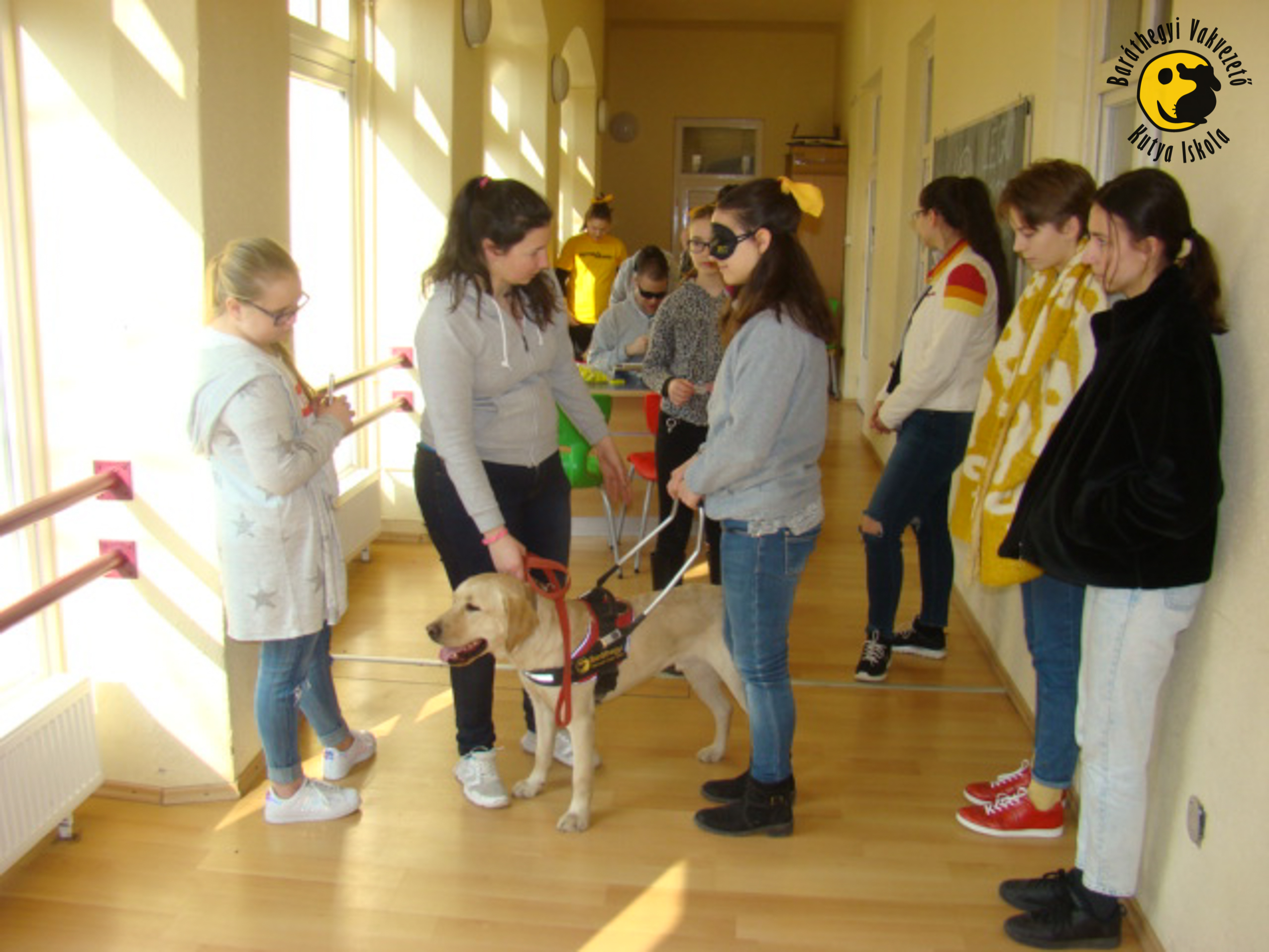 Az iskola épületéből indulunk sétára egy diáklánnyal, aki éppen most hallgatja meg az instrukciókat a vakvezető kutyás közlekedésről